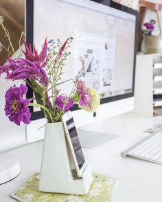 a computer monitor sitting on top of a desk next to a vase with flowers in it