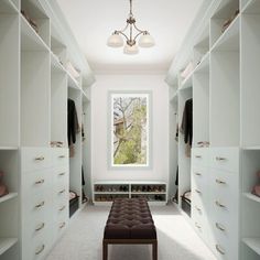 a walk - in closet with white cabinets and drawers, an upholstered bench