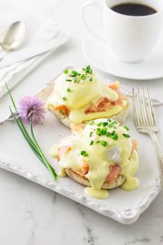 two open sandwiches on a plate with sauce and green garnish next to a cup of coffee