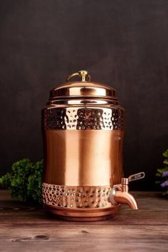 a copper colored pot with a handle on top of a wooden table next to flowers