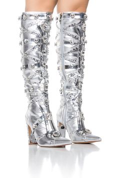 Kick your look into high gear with The AZALEA WANG Speed Drive Silver Embellished Boot. This ultra luxe silver metallic boot features a faux leather fabrication, a pointed toe silhouette, rhinestone-embellished detailing, metallic faux leather trim accents, a diamond-studded chunky heel, and a knee-height shaft. Complete with a classic inner ankle zipper closure and strappy patent detailing throughout. Style with a sleek catsuit and a faux leather jacket for a complete look. (all measurements approximate from size 7.5) - Faux Leather Upper - Pointed Toe - Knee High Shaft - Chunky Heel - 16” Shaft Height - 4” Heel Height - Imported Product ID: 365777 Azalea Wang Boots, Metallic Boots, Boot Bling, Azalea Wang, Faux Leather Jackets, Chunky Heel, Diamond Studs, Chunky Heels, Knee High Boots