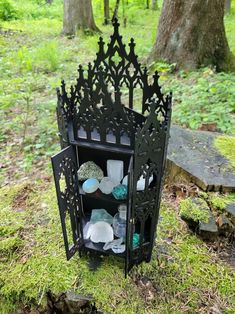 a black shelf with glass and rocks on it in the grass next to some trees