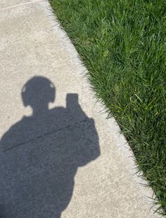 the shadow of a person holding a cell phone in front of their face on a sidewalk