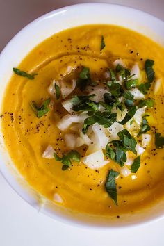 a white bowl filled with yellow soup and garnished with parsley on top