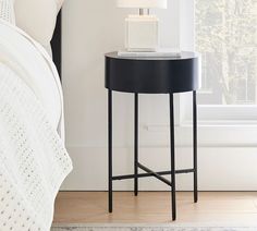 a black table with a lamp on it next to a white bed in a bedroom