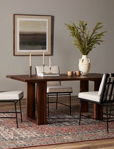 a dining room table with chairs and a vase on the rug in front of it