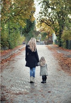 a mother and her child walking down a path in the fall with leaves on the ground