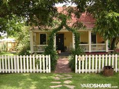 a white picket fence surrounding a small house with flowers on the front door and windows