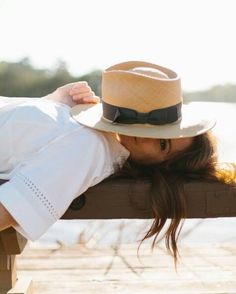 a woman wearing a hat leaning on a fence with her head resting on the rail