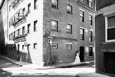 a bride and groom standing in front of a tall brick building on a city street