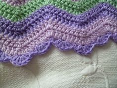 there is a crocheted blanket on top of a white bed sheet with purple, green and blue stripes