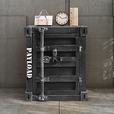 an old metal box with a clock and books on top sits in front of a concrete wall