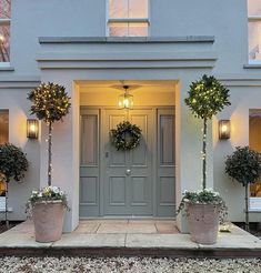 two potted plants are in front of a house with lights on the windows and doors