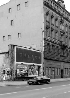 an old black and white photo of a car driving down the street in front of a building