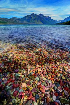 a painting of rocks on the shore of a mountain lake with mountains in the background