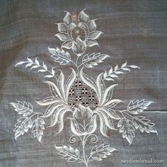 an embroidered piece with white flowers and leaves on grey linen fabric, close up view