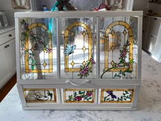 a cabinet with stained glass doors and flowers on the front, sitting on a marble countertop