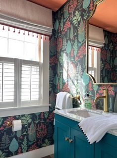 a bathroom with floral wallpaper and blue cabinetry, gold faucet, white sink, and window