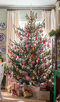 a decorated christmas tree in the corner of a room with plates on the wall and windows