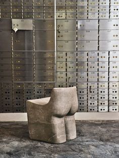 a chair made out of concrete sitting in front of a wall with lots of mail boxes