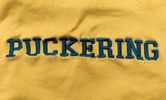 the word puckering written in blue ink on a yellow sweatshirt with green lettering and black stitching