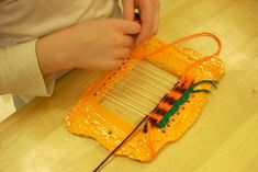 a person is working with an orange and green weaving loom on a wooden table