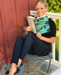 a woman sitting in a chair reading a book on the porch with her legs crossed