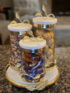 three glass jars filled with candy and nuts on top of a marble counter next to a gold plate