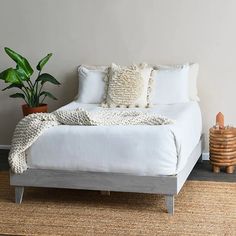 a bed with white sheets and pillows on top of it next to a potted plant