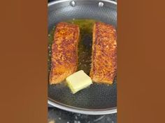 two pieces of fish cooking in a frying pan with butter on the side,