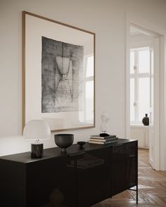 a black cabinet in a white room with an art piece on the wall above it