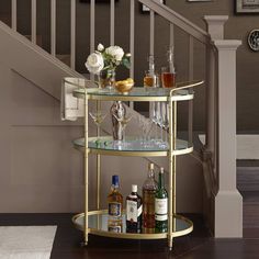 a bar cart with wine glasses and liquor bottles on it in front of a stair case