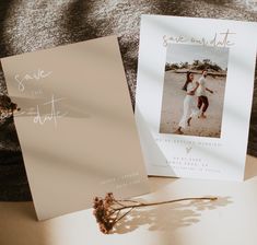 two wedding save the dates cards on top of a bed next to a dried flower