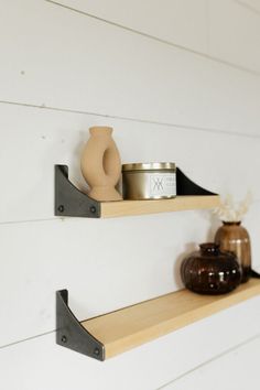 two shelves with candles and vases on them against a white painted wall in a room