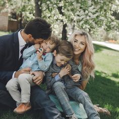 a man, woman and two children are sitting on the grass in front of a tree