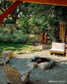 a fire pit in the middle of a yard with chairs around it and trees behind it