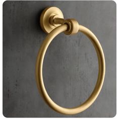 a gold colored towel ring on a gray wall with concrete flooring and cement walls in the background