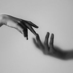 two hands reaching out towards each other in black and white photo with shadow on wall