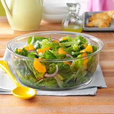 a salad in a glass bowl with oranges, onions and lettuce on the side