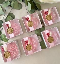 four small pink boxes with gold coins in them on a table next to some flowers