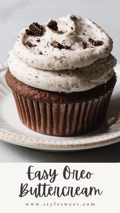 a chocolate cupcake with white frosting and oreo cookies on top is sitting on a plate