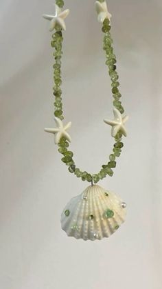 a necklace with green beads and white starfishs on it's sides, hanging from a silver chain