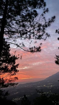 the sun is setting behind some trees on top of a hill with mountains in the background