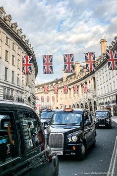 cars are driving down the street with flags hanging from buildings in the backgroud