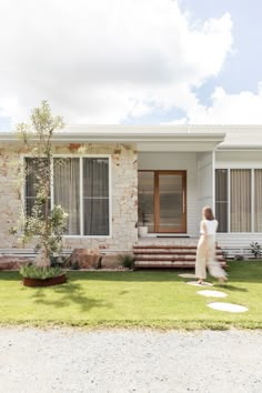 a woman is walking in front of a house with grass and rocks on the lawn