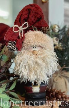 a santa clause doll sitting on top of a table next to pine cones and other christmas decorations