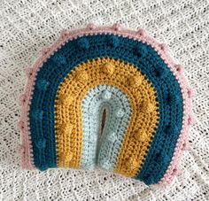 there is a crocheted pot holder with a rainbow design on the top and bottom