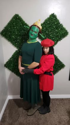 two people in costumes standing next to each other with green plants on the wall behind them