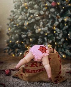 a baby laying on top of a bag in front of a christmas tree