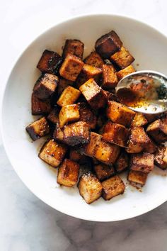 a white bowl filled with fried tofu and a spoon on top of the bowl